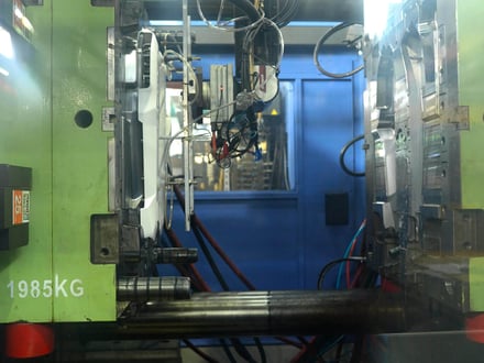 1,985 kg の金型を取り付け、プラテン間で型開きした状態の AMP 射出成形機。キャビティ側とコア側、冷却および油圧の配管が確認できる。