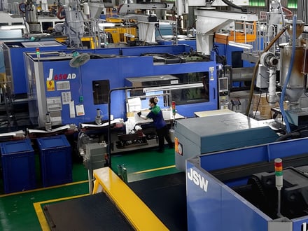 成形機脇の作業ステーションで、成形部品の検査、バリ取り、梱包を行う AMP のオペレーター。直接出荷に対応している。